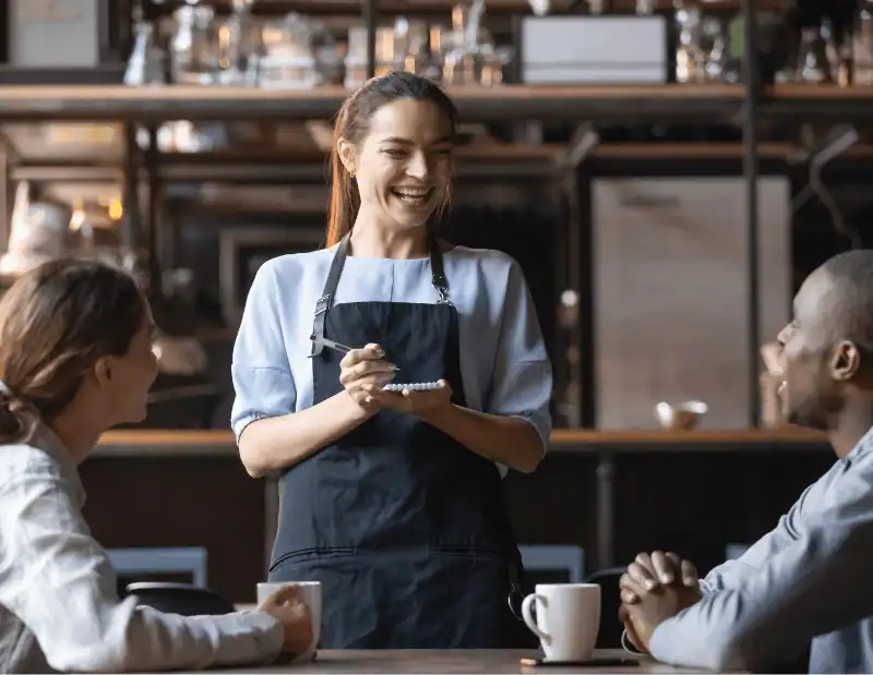 A smiling waitress takes the order of two happy diners in a cosy restaurant